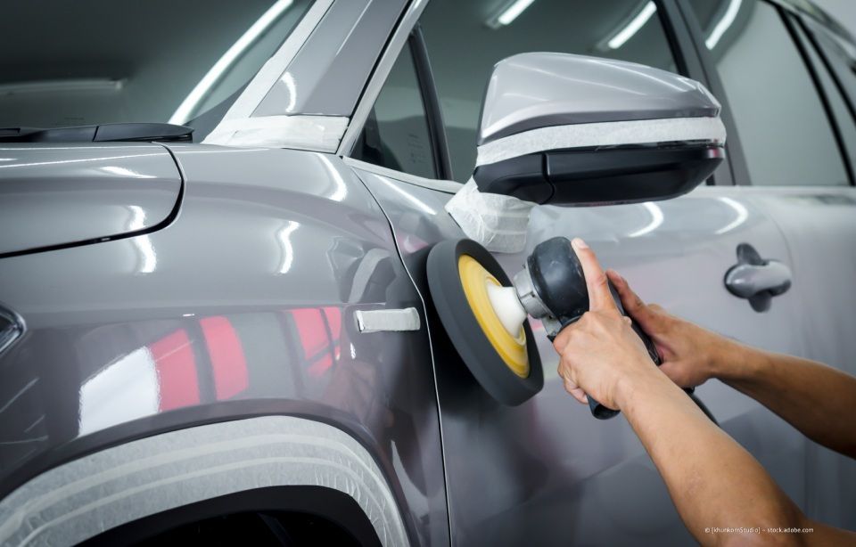 Ein graues Auto wird in einer Autolackiererei mit einer Poliermaschine poliert.