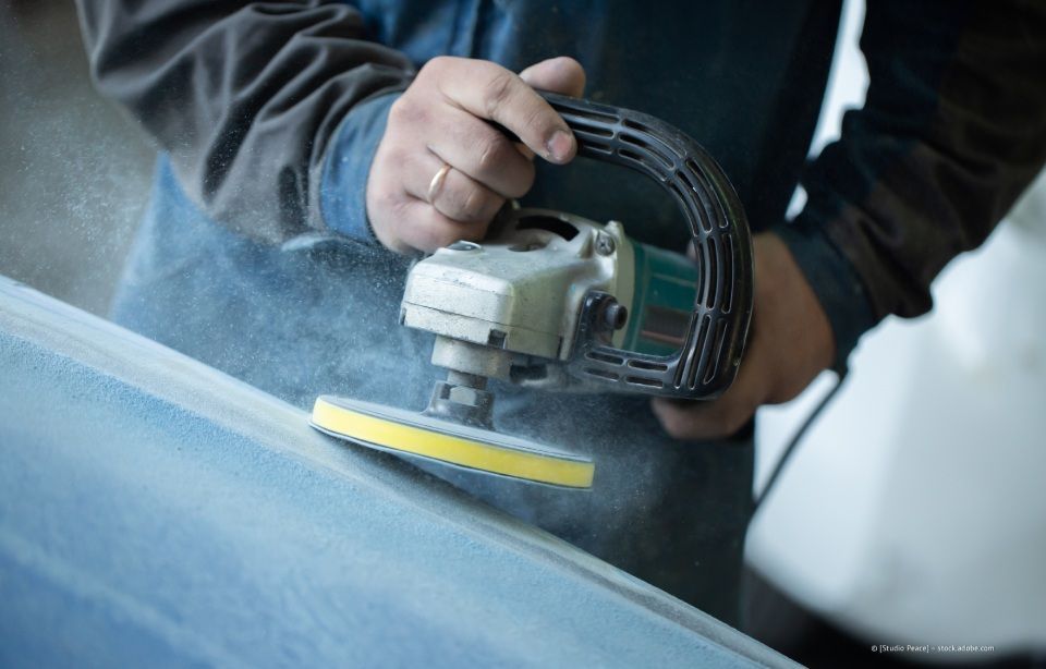 Eine Person benutzt einen handgeführten Elektroschleifer auf einer blauen Oberfläche; Staub ist sichtbar.