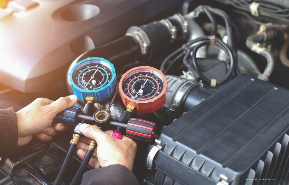 Hände prüfen mit blauen und roten Manometern den Kühlmittelstand im Motorraum.