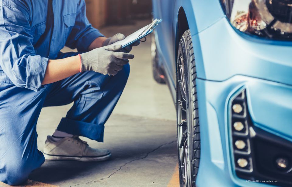 Ein Mechaniker überprüft in einer Garage mit einem Reifendruckmesser das Vorderrad eines blauen Autos.
