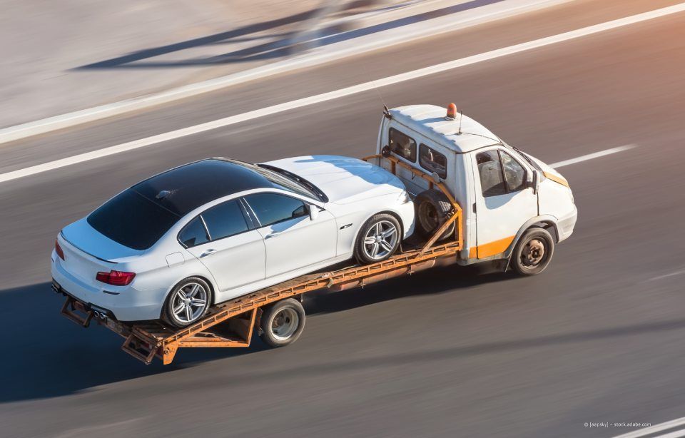Ein weißer Pkw auf einem orangefarbenen Abschleppwagen fährt auf einer Autobahn