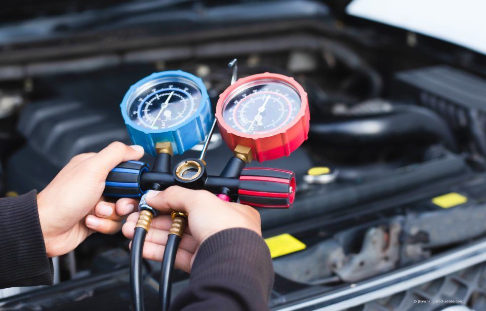 Hände halten blaue und rote Kfz-Klimaanlagenanzeigen über einem offenen Motorraum