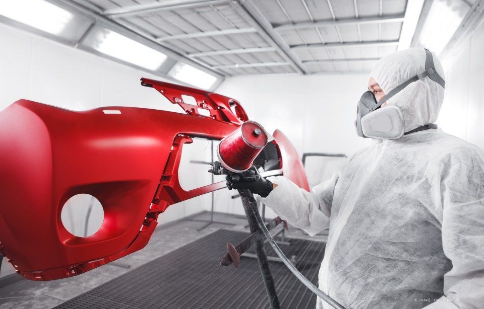 Ein Arbeiter lackiert eine rote Autokarosserie in einer weißen Autolackiererei.