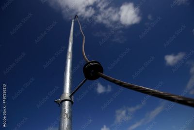 Silberner Mast mit einem Kabel vor einem blauen Himmel mit ein paar weißen Wolken.