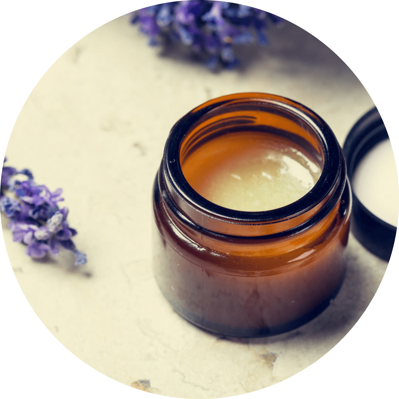 Un tarro de crema está sobre una mesa al lado de flores moradas.