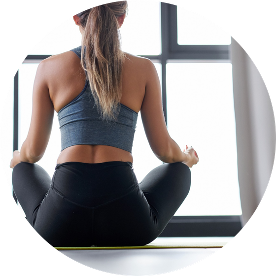 Una mujer está sentada en una esterilla de yoga frente a una ventana.