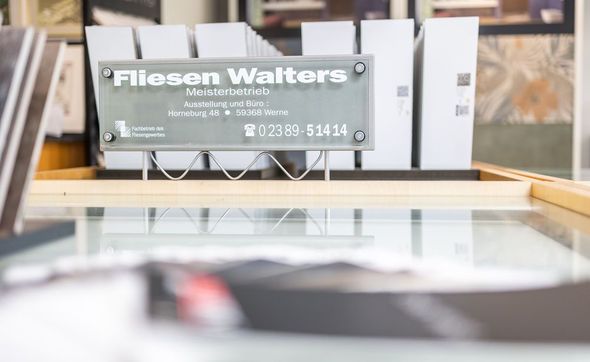 Auf einem Glastisch steht ein Schild mit der Aufschrift „Fliesen Walters“.