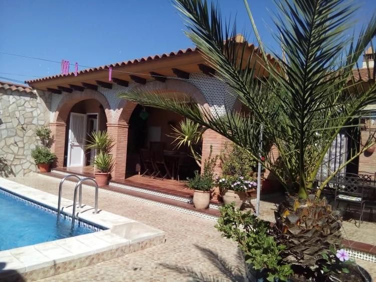 Villa junto a la piscina con arcos de ladrillo rojo, palmeras y cielo azul claro.
