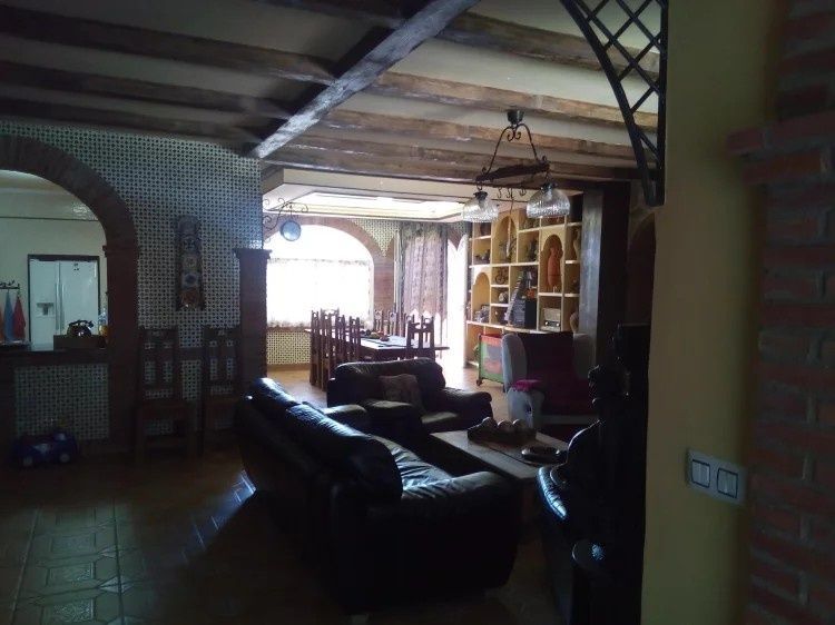Interior de sala de estar con sofá de cuero oscuro, puertas arqueadas, vigas de madera y un comedor.