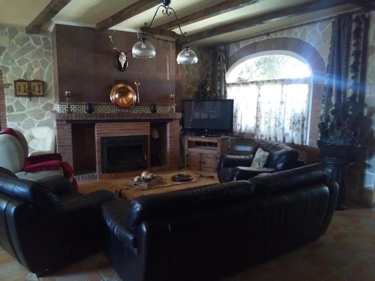 Acogedora sala de estar con chimenea, sofás de cuero oscuro, TV y gran ventanal arqueado.