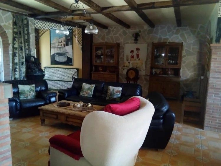 Sala de estar con muebles de cuero, pared de piedra, vigas de madera y decoración antigua.