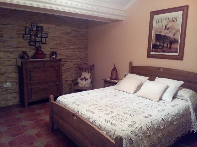 Dormitorio con cama, cómoda, silla y póster en la pared. Tonos beige y marrón.