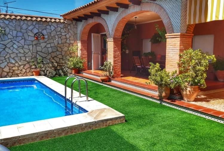 Patio trasero con piscina, patio con arcos y césped artificial.