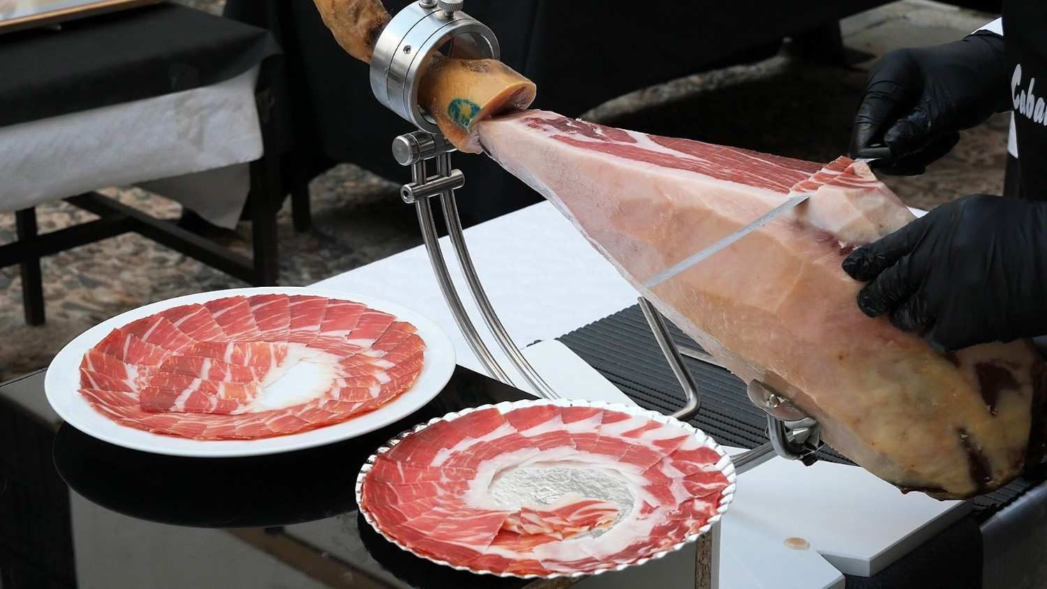 Una persona cortando jamón ibérico de una pierna sobre un soporte, servido en forma de espiral en platos.