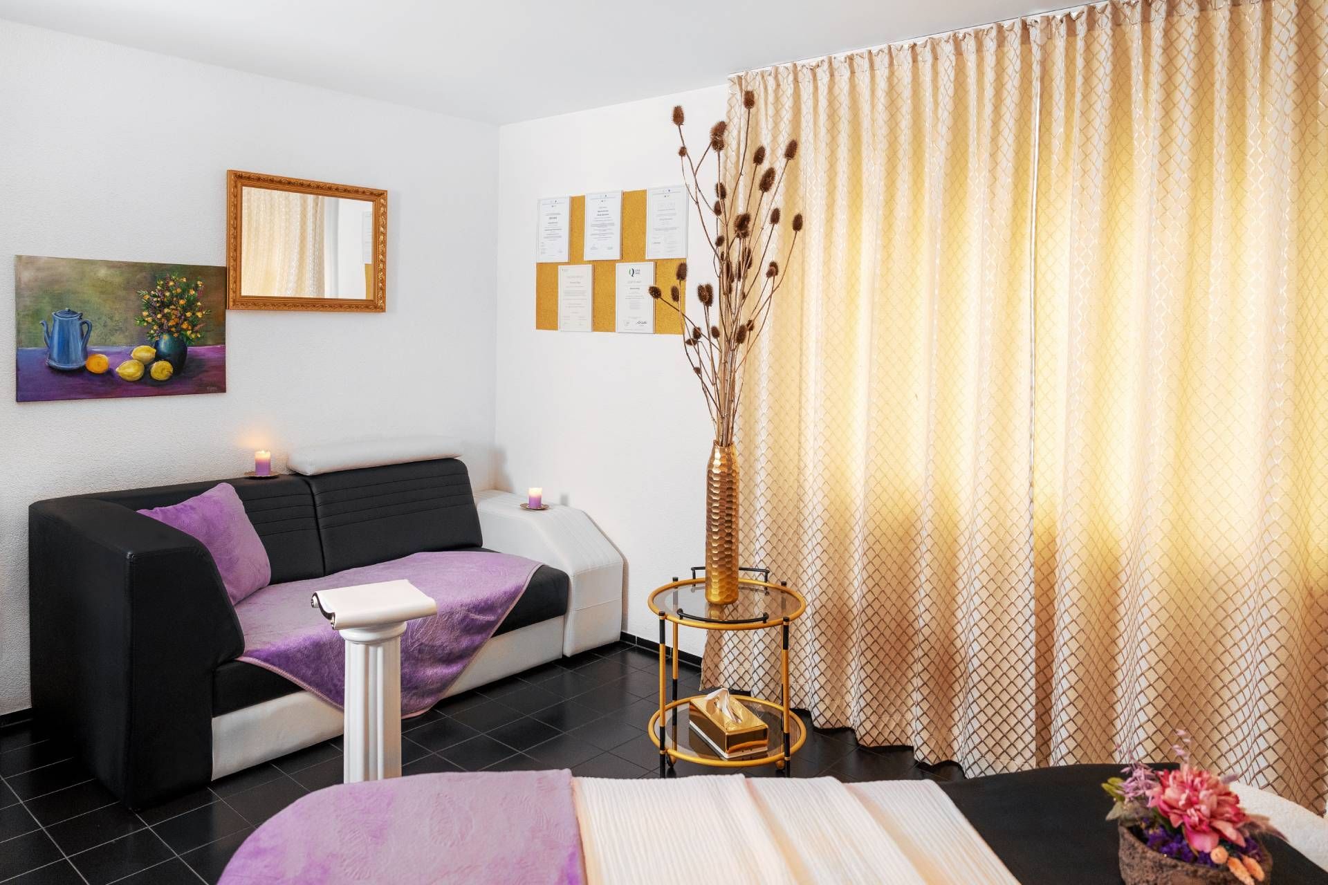 Modernes Wohnzimmer mit schwarzem Sofa, violetten Akzenten, geblümten Vorhängen und warmer Beleuchtung
