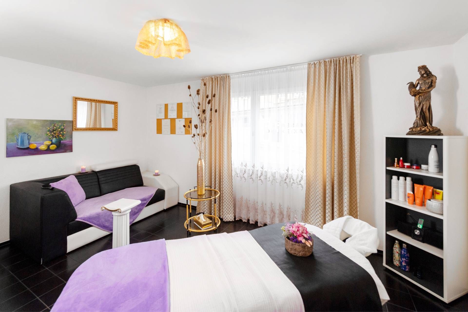 Helles Schlafzimmer mit schwarz-lila Bett, passendem Sofa, Bücherregalen und grossem, mit Vorhängen versehenem Fenster