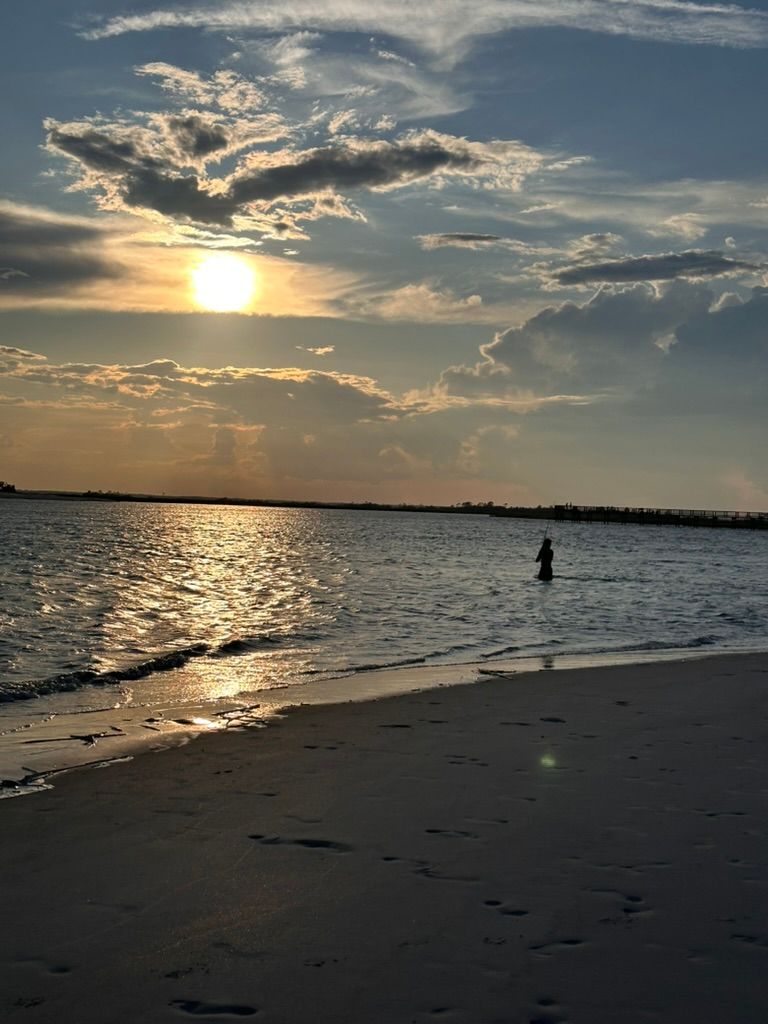 Three people playing on a sandy beach at sunset, with a calm sea and island in the background.