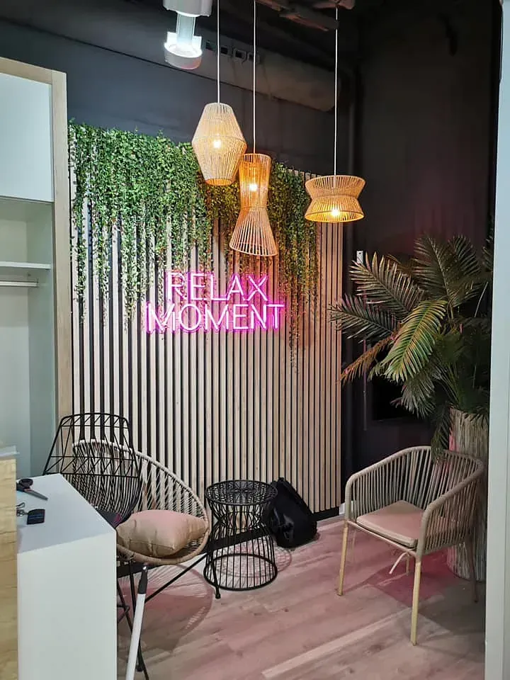 Interior acogedor con letrero de neón "MOMENTO DE RELAX", luces colgantes, sillas y decoración de pared verde.