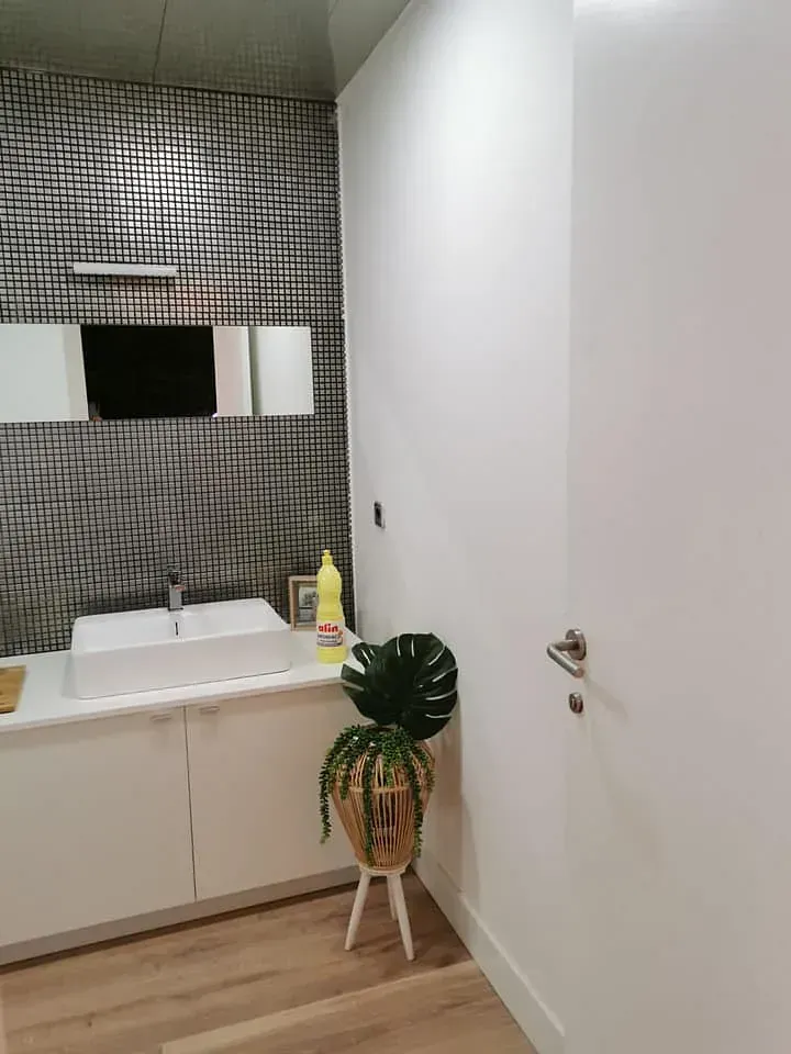 Baño blanco moderno con lavabo, pared estampada y planta en maceta.