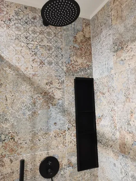 Ducha con azulejos estampados, cabezal de ducha negro y controles negros.