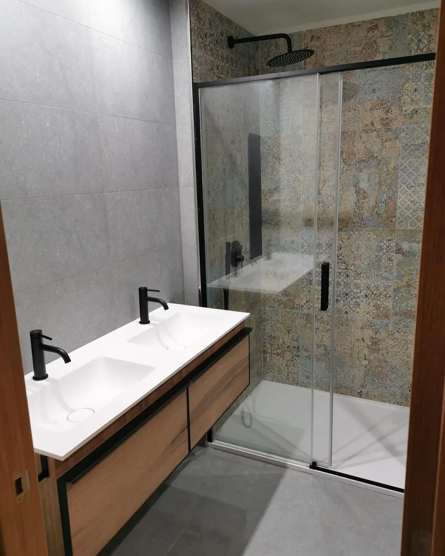 Baño moderno con tocador flotante de madera y ducha de cristal.