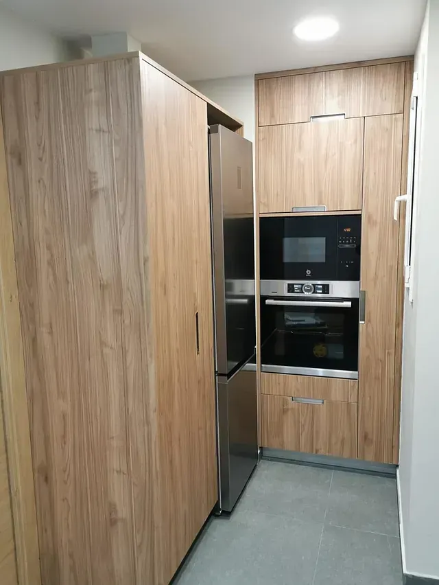 Cocina con gabinetes de madera clara, refrigerador y horno de acero inoxidable, piso de baldosas grises.