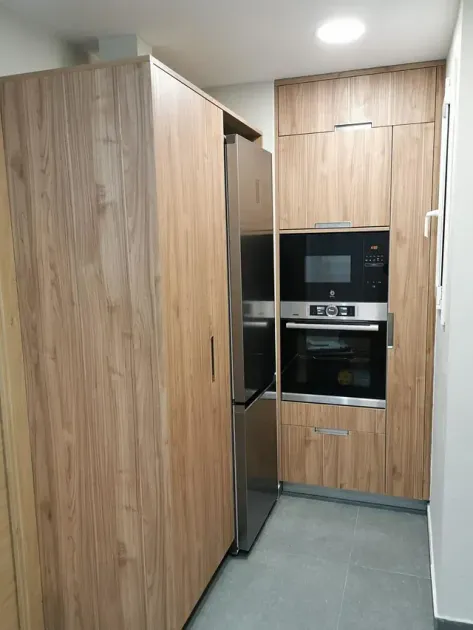Cocina con gabinetes de madera clara, refrigerador y horno de acero inoxidable, piso de baldosas grises.