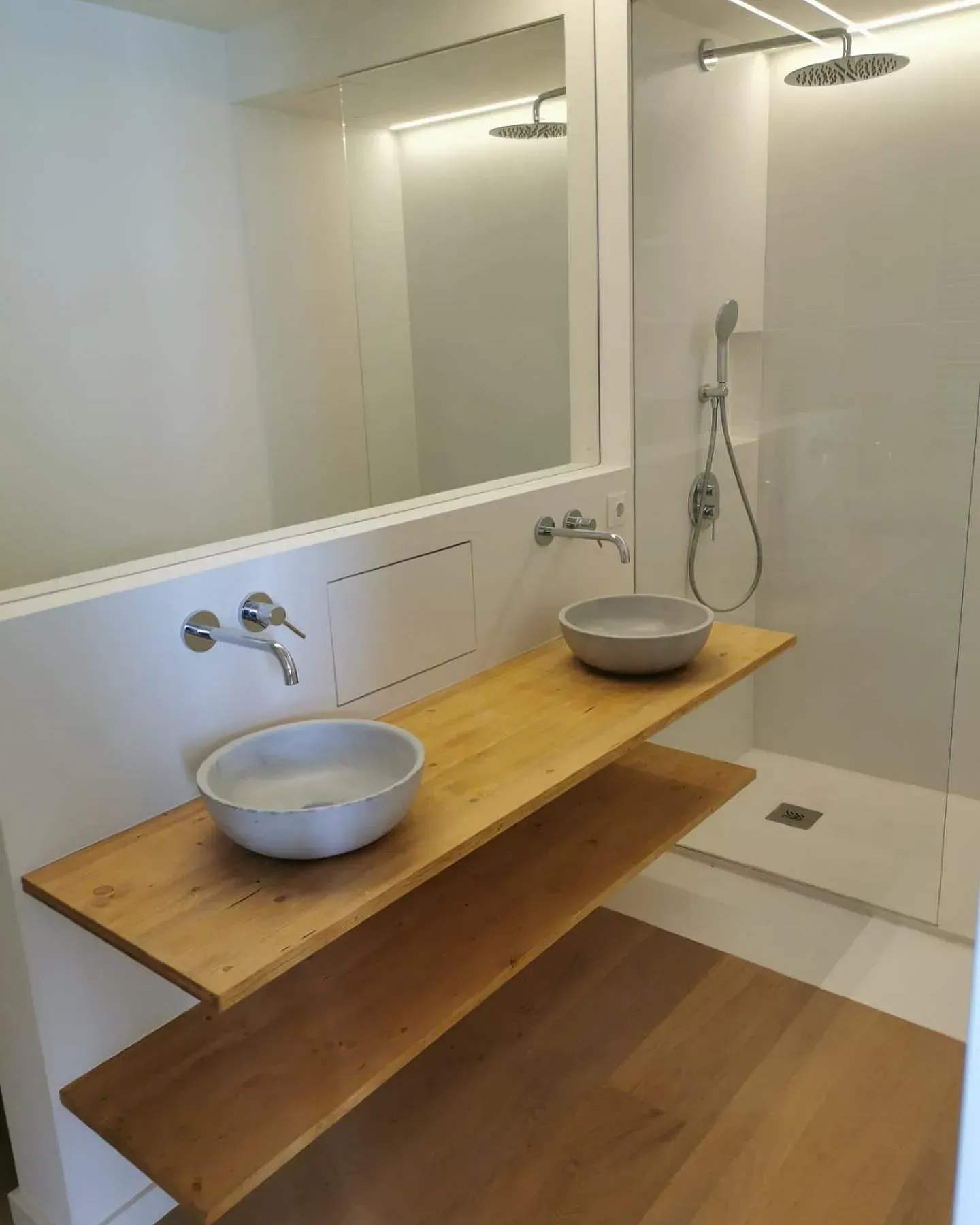 Baño moderno con dos lavabos sobre estantes de madera, ducha y un gran espejo.