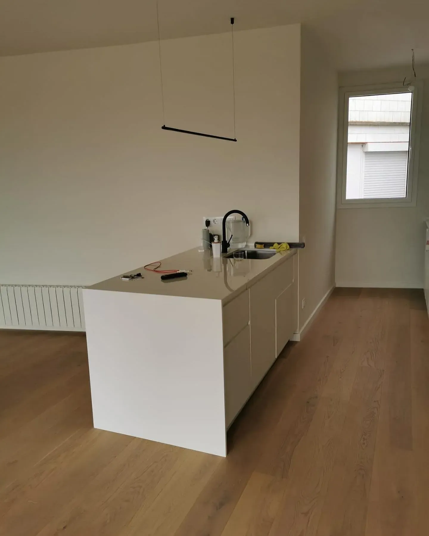 Isla de cocina blanca con fregadero y encimera en una habitación con pisos de madera y una ventana.