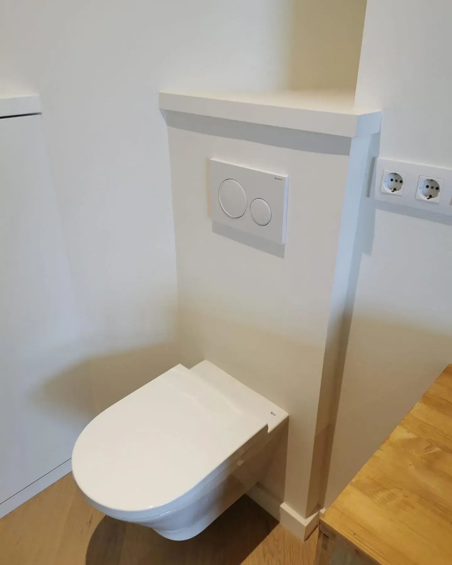 Inodoro blanco moderno en una habitación pequeña con paredes blancas y molduras de madera. Cisterna con pulsador.