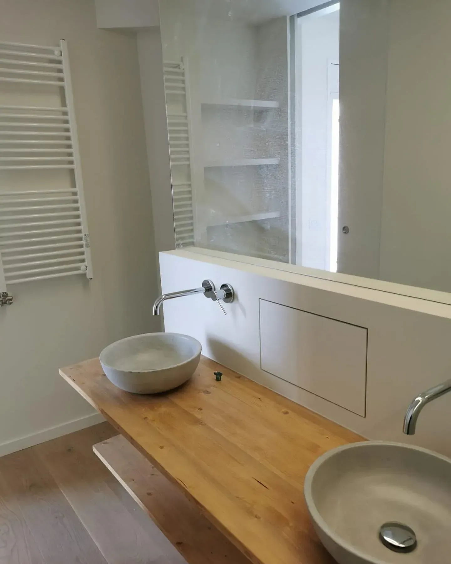 Baño con tocador de madera, lavabos redondos, accesorios blancos y un espejo grande.