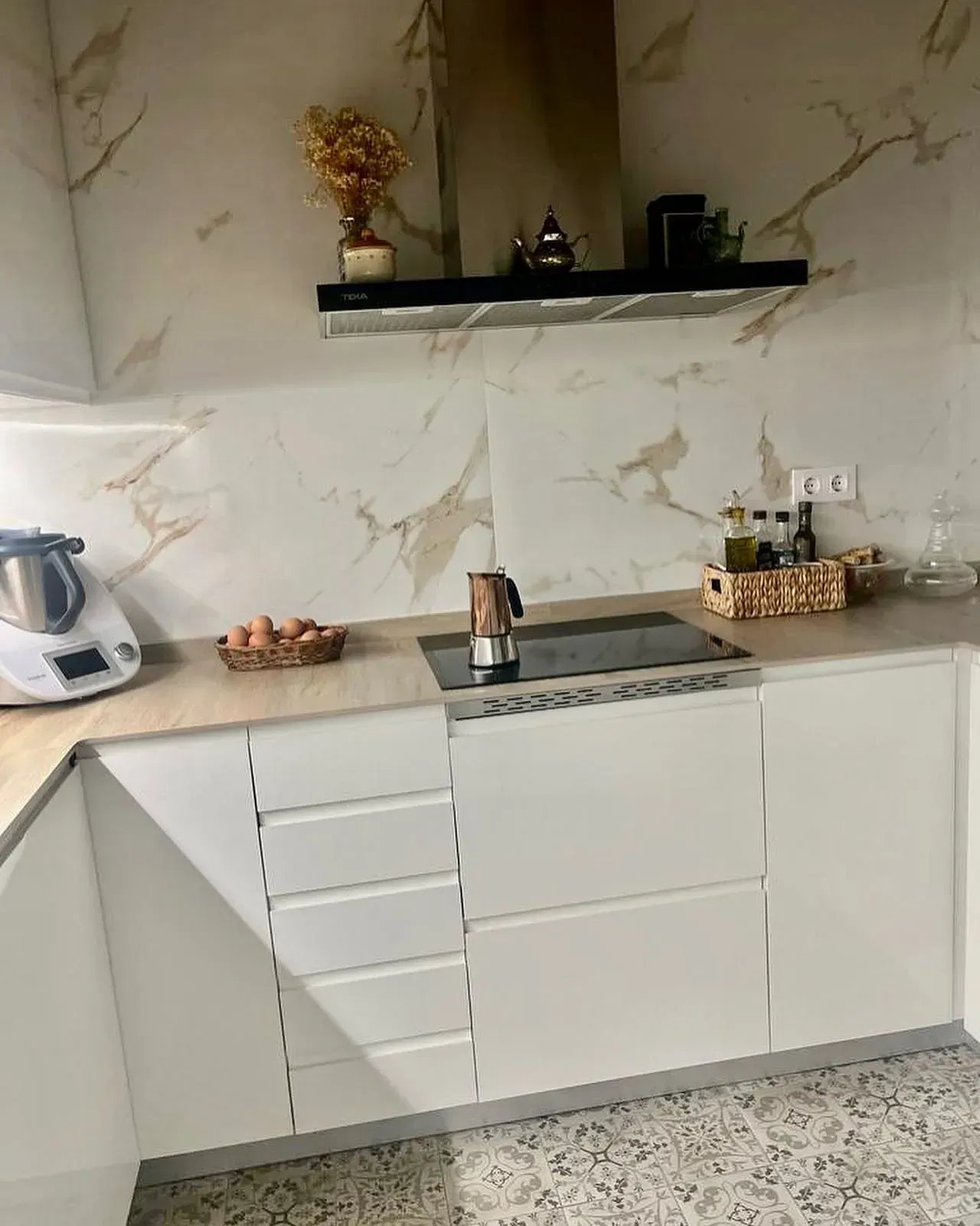 Cocina blanca moderna con salpicadero de mármol, encimeras de madera y hervidor de cobre.