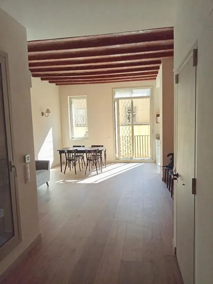 Comedor luminoso con vigas de madera, mesa, sillas y balcón; pisos y paredes de madera clara.