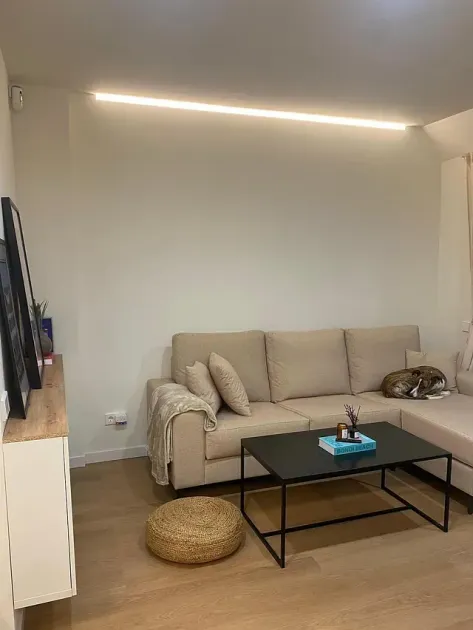 Una acogedora sala de estar con un sofá beige, una mesa de café negra y un gato durmiendo.
