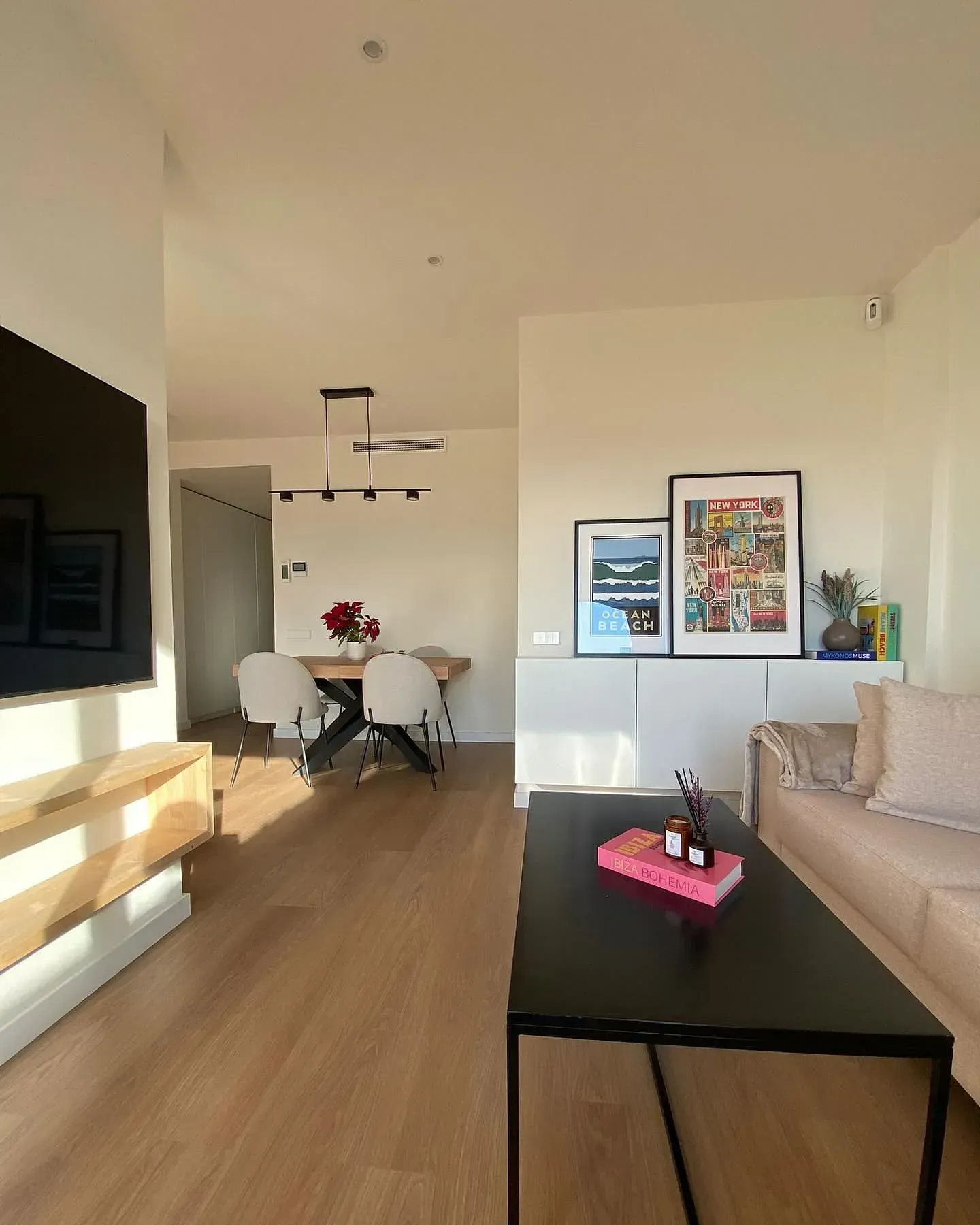 Sala de estar con mesa, sofá y obras de arte; pisos de madera y paredes neutrales.