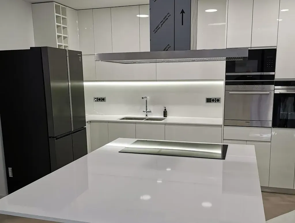 Cocina blanca moderna con isla, electrodomésticos de acero inoxidable y refrigerador negro.