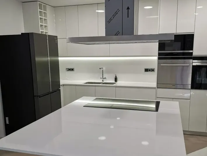 Cocina blanca moderna con isla, electrodomésticos de acero inoxidable y refrigerador negro.