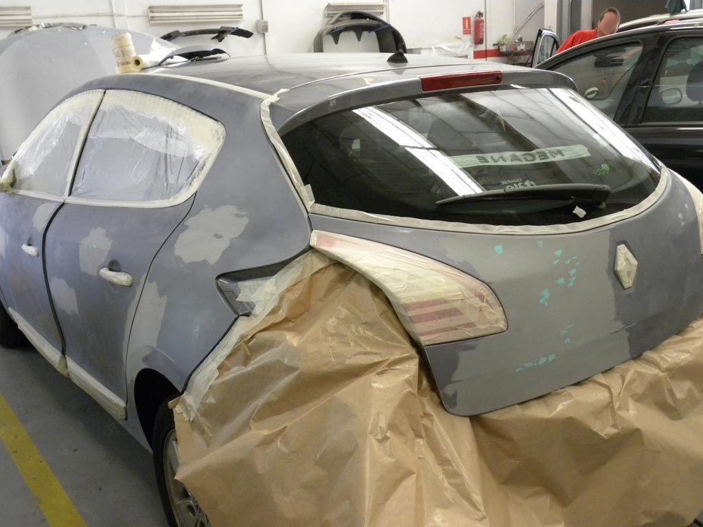 Coche en reparación en un taller de carrocería, enmascarado para pintar.