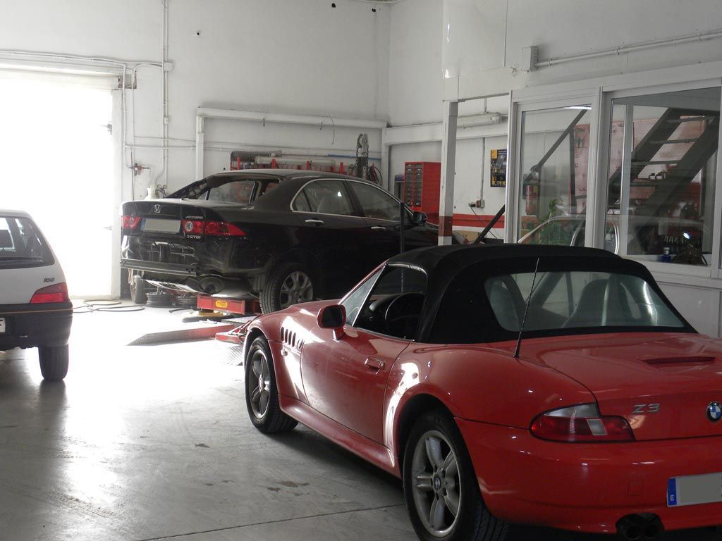 Descapotable rojo y coche negro dentro de un garaje; puerta abierta visible.
