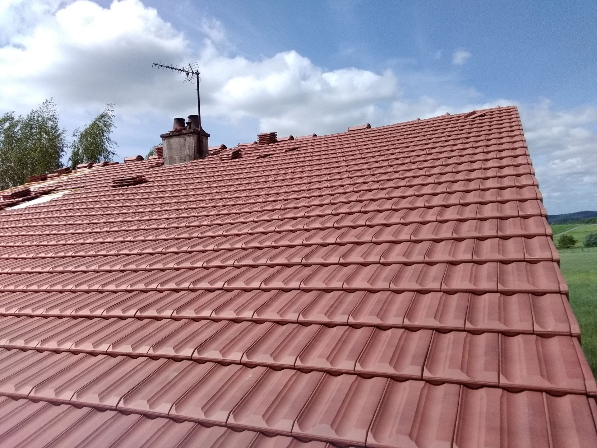 Toit de tuiles rouges sur un bâtiment avec cheminée et antenne.