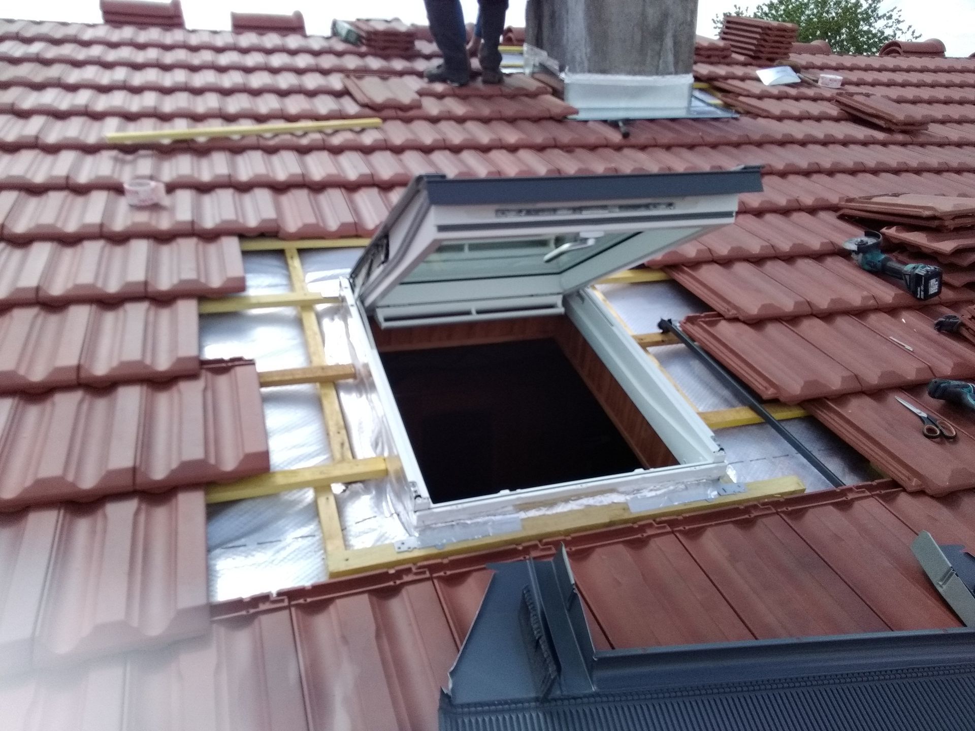 Installation d'une toiture : puits de lumière en cours de réalisation entouré de tuiles et de poutres en bois.