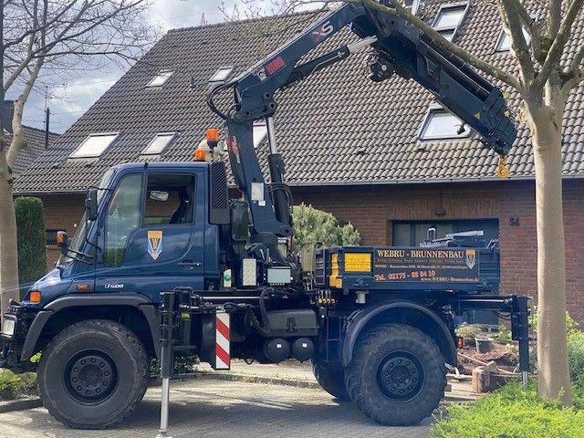 Ein blauer Lastwagen mit einem Kran auf der Ladefläche steht vor einem Haus.