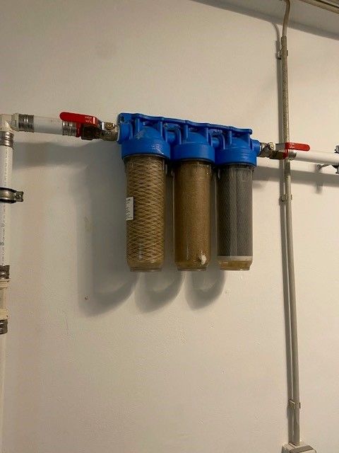 Ein Wasserfilter hängt neben einem Rohr an der Wand.