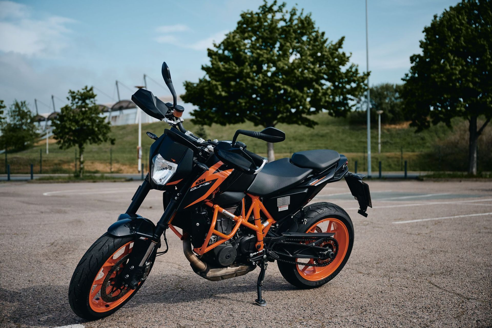 Schwarz-orangefarbenes KTM Duke-Motorrad, auf Asphalt vor Bäumen geparkt.