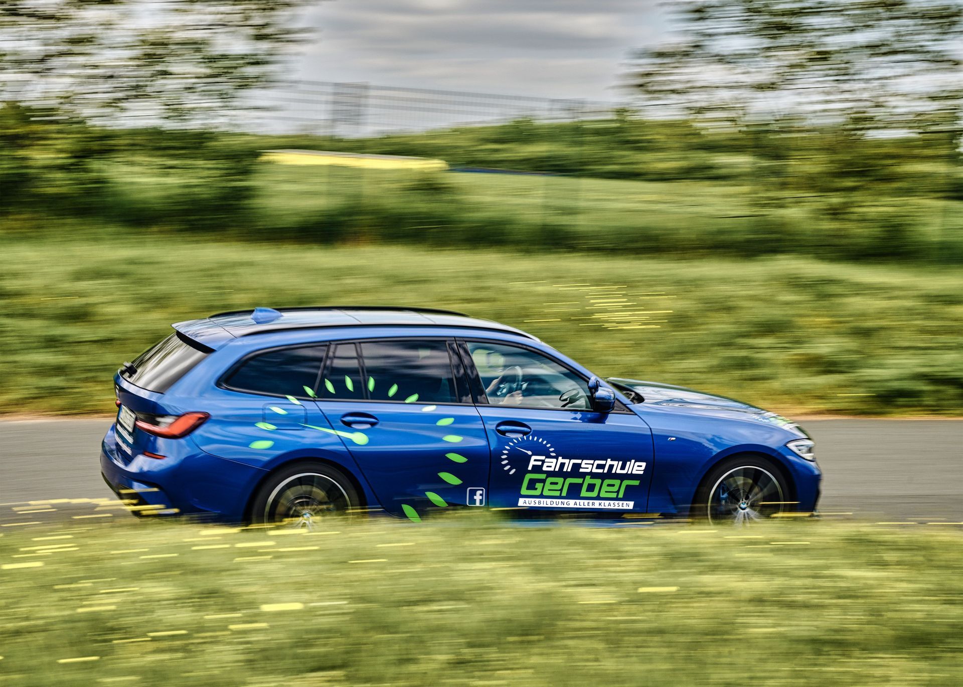 Blauer BMW-Kombi rast auf einer Rennstrecke, mit grün-weißem Logo an der Seite, unscharfer Hintergrund.