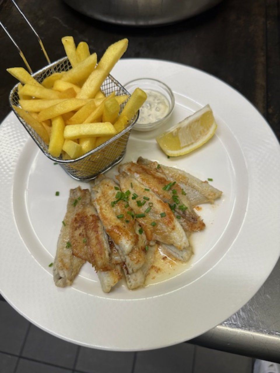 Assiette de filets de poisson frits, frites dans un panier métallique, quartier de citron et sauce à tremper.