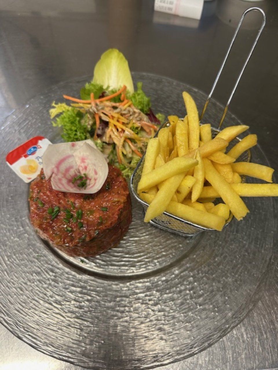 Steak tartare avec frites et salade sur assiette transparente. Sauce incluse.