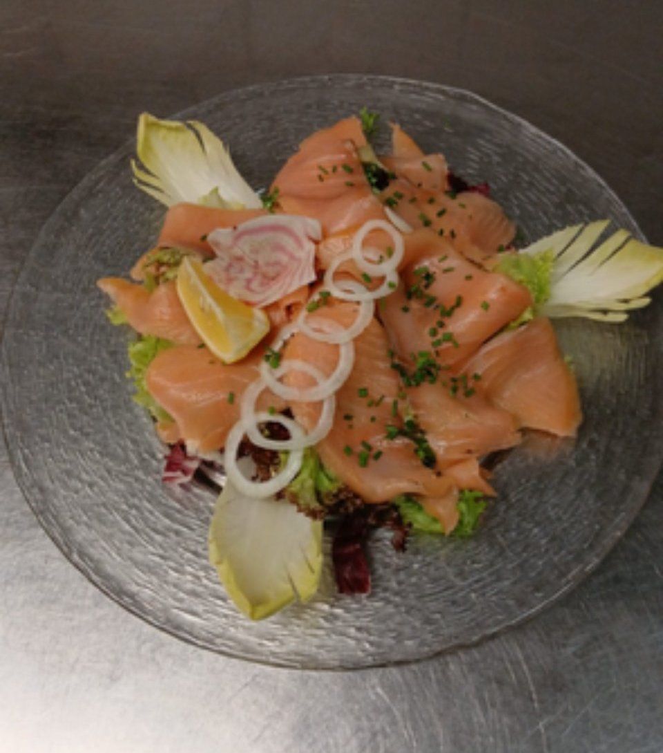 Salade de saumon fumé sur une assiette transparente, garnie de rondelles d'oignon, de citron et d'endives.