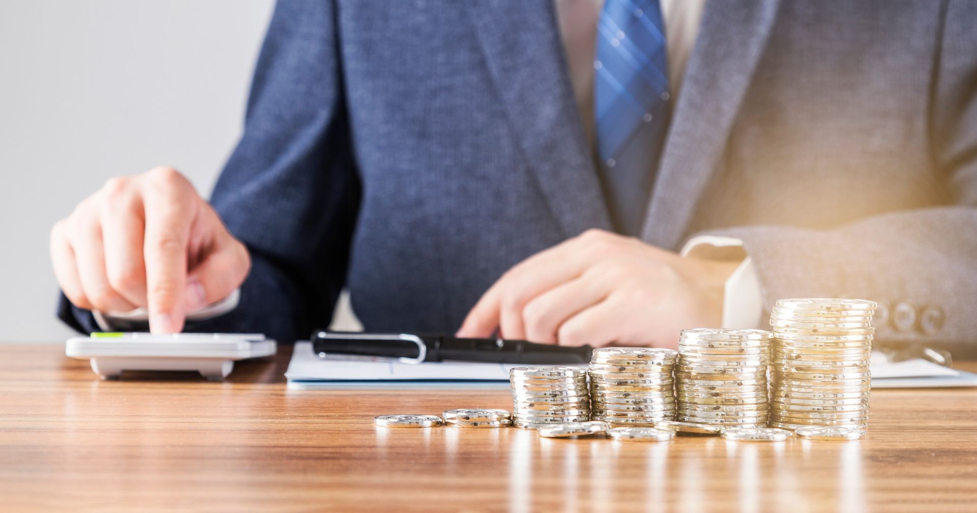 Un hombre con traje y corbata está sentado en una mesa usando una calculadora.