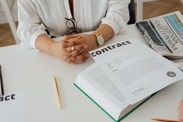 Una mujer está sentada en una mesa con un libro y un contrato.